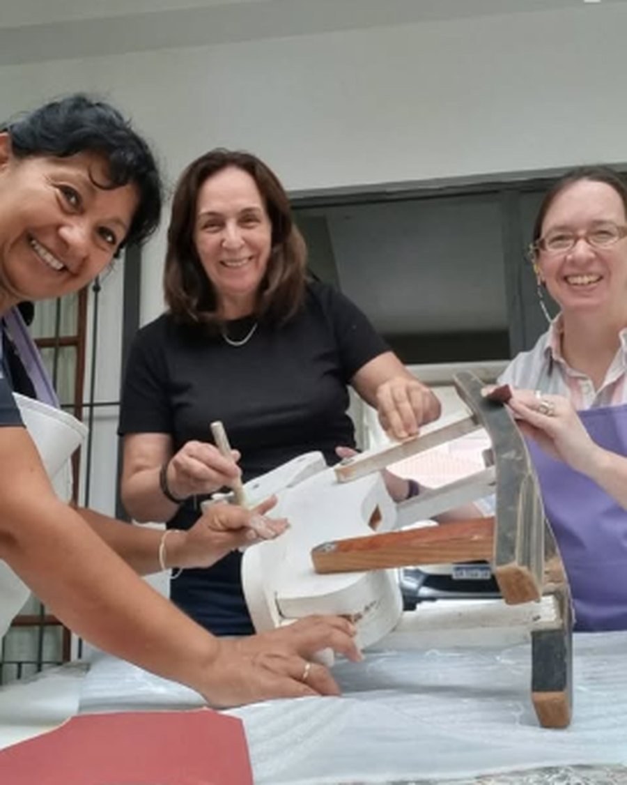 Tres alumnas sonriendo mientras restauran un mueble