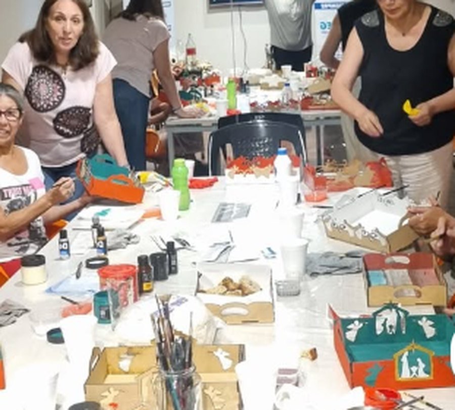 Mesa larga con grupo pintando cajitas de madera en un taller de Navidad