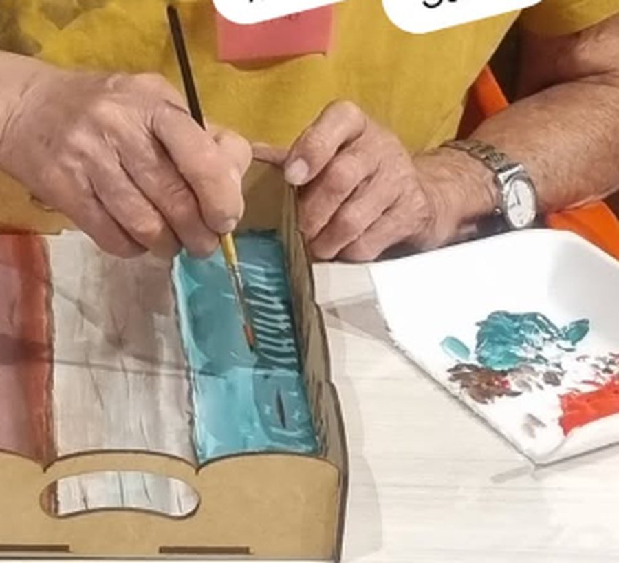 Manos pintando con pincel una pieza de madera con pintura celeste